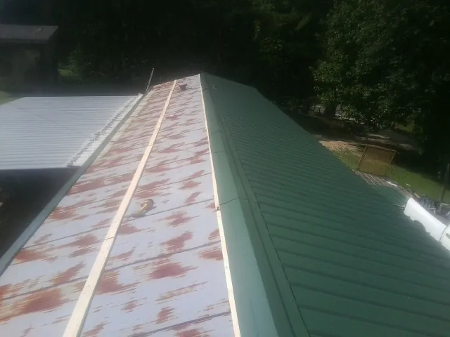 Old rusted panels beside newly installed green metal roofing — Wind Damage Roof Repair by Roofing Brothers in Wynnewood