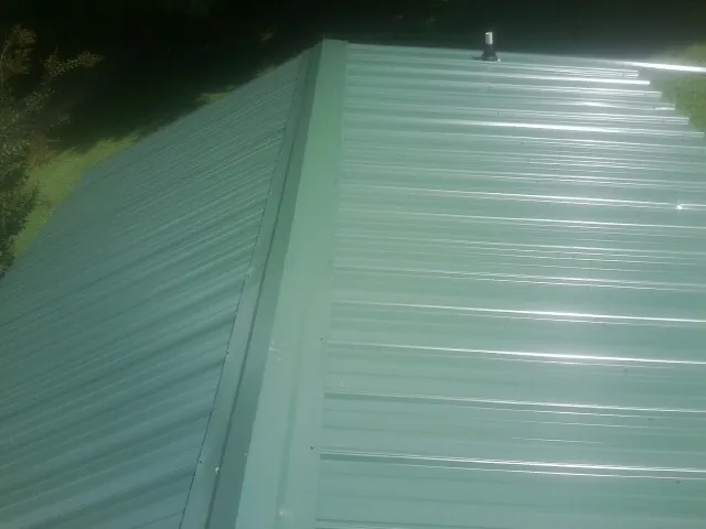 New green metal panels meeting at the ridge of a roof — Flat Roof Repair work by our crew in Wynnewood