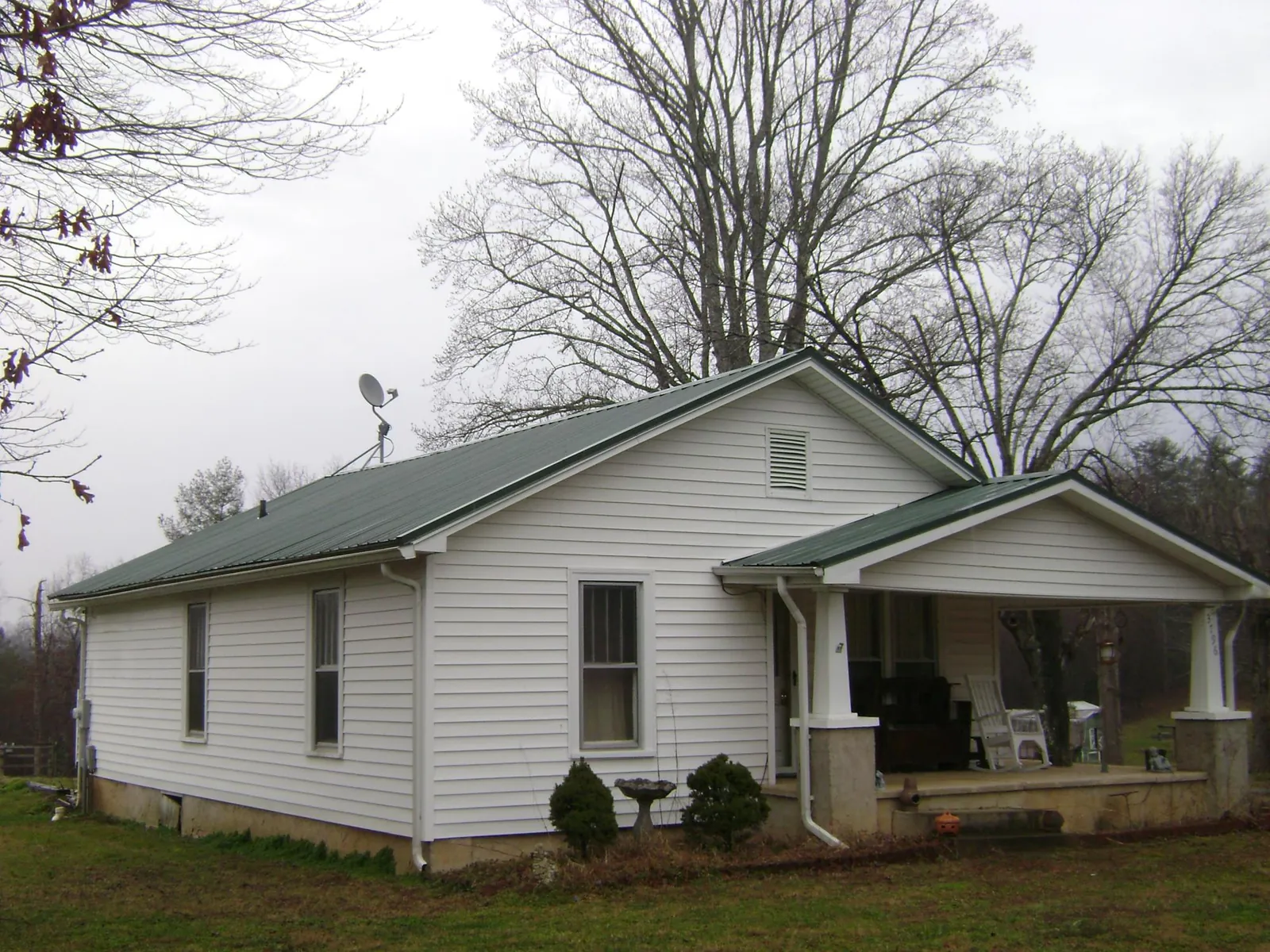 Green metal roof on a white bungalow with a side porch in Wynnewood