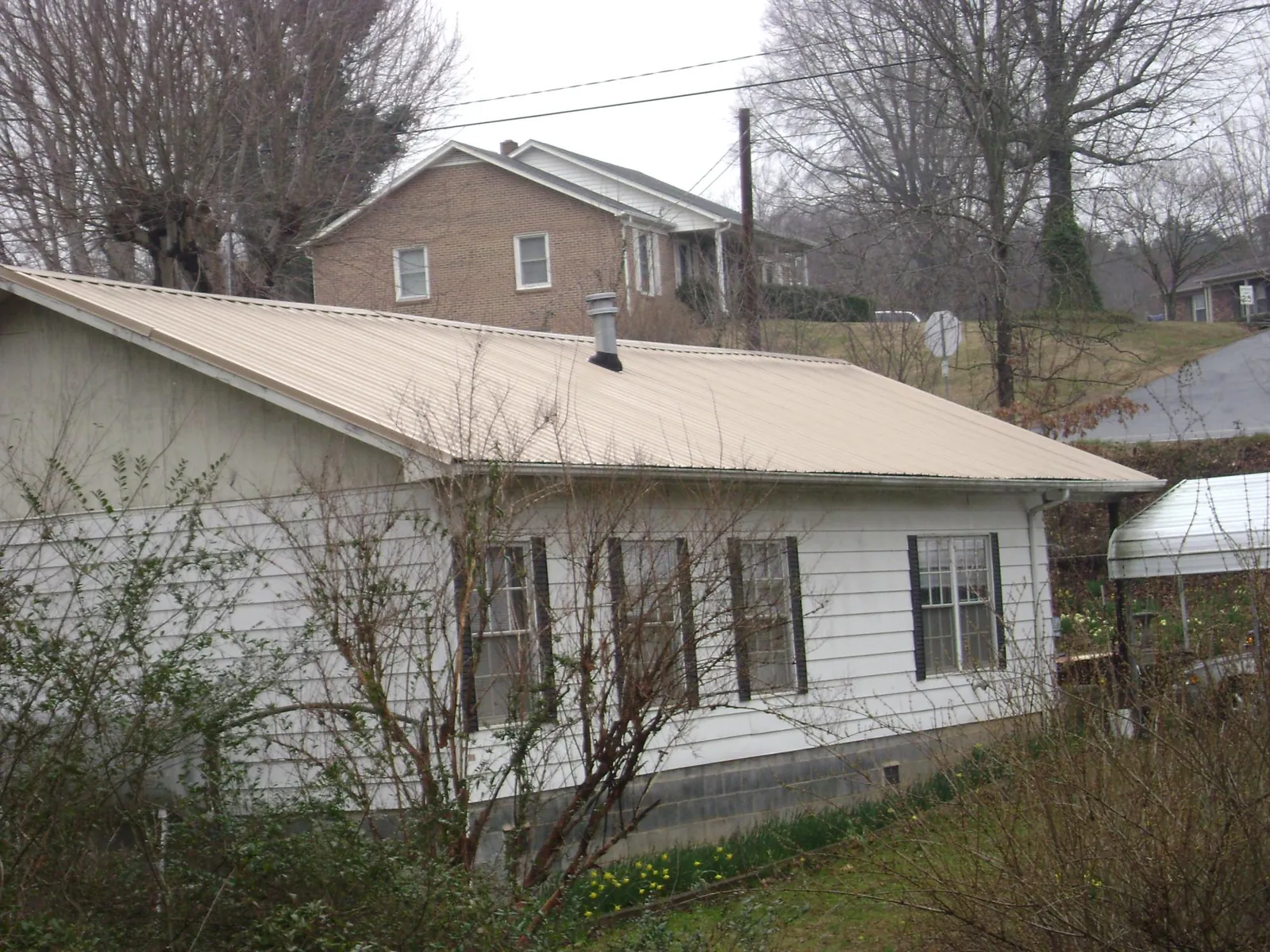 Tan metal roof on a white sided house set into a hillside — Commercial Roofing by Roofing Brothers in Wynnewood