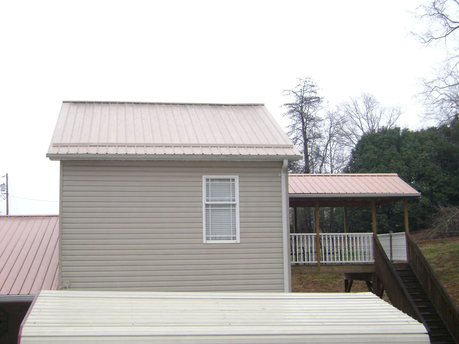 Tan metal roofs on a two story addition and attached porch, from a Roof Replacement job in Wynnewood